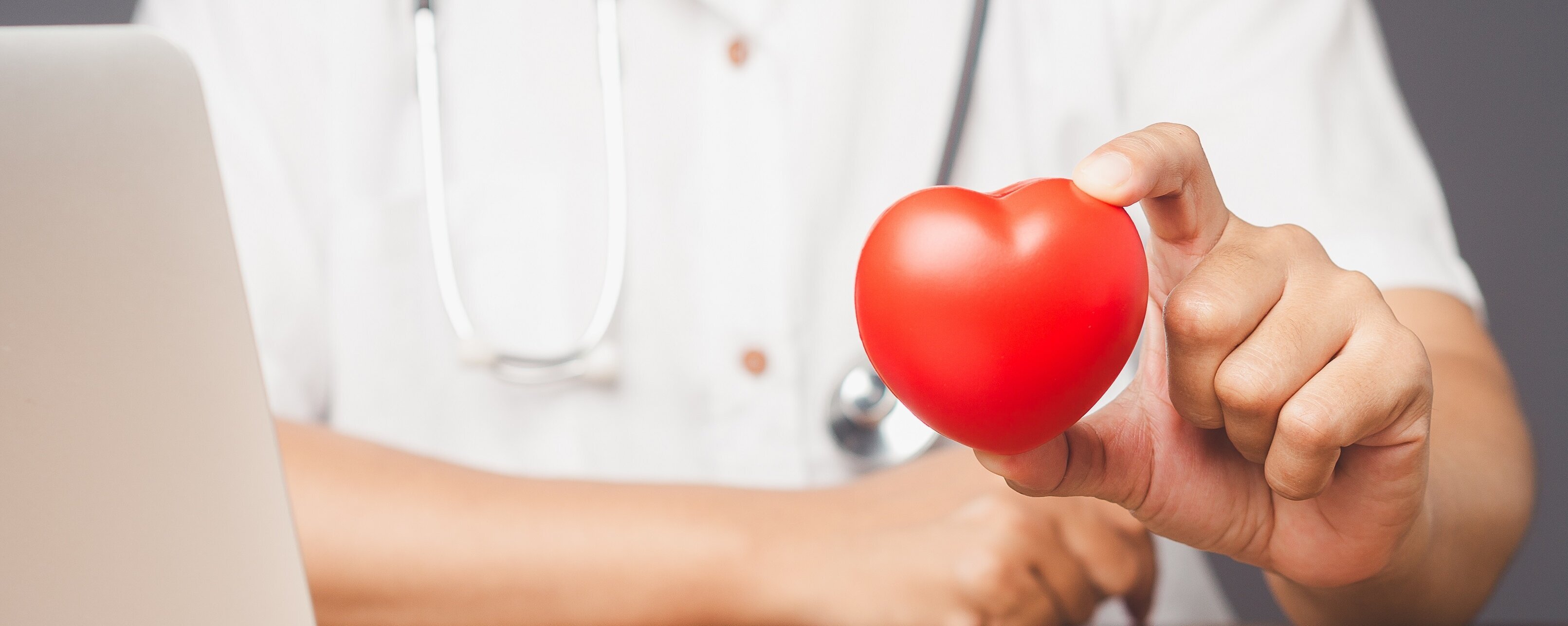 Ein Arzt sitzt vor einem Laptop und hält ein Herz hoch.
