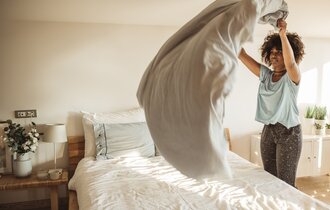Eine Frau schüttelt die Bettdecke auf einem Bett auf.