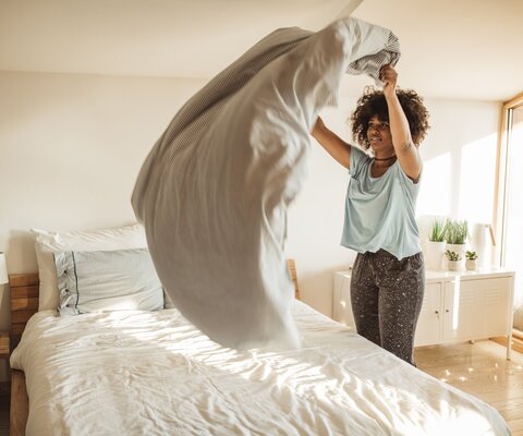 Eine Frau schüttelt die Bettdecke auf einem Bett auf.