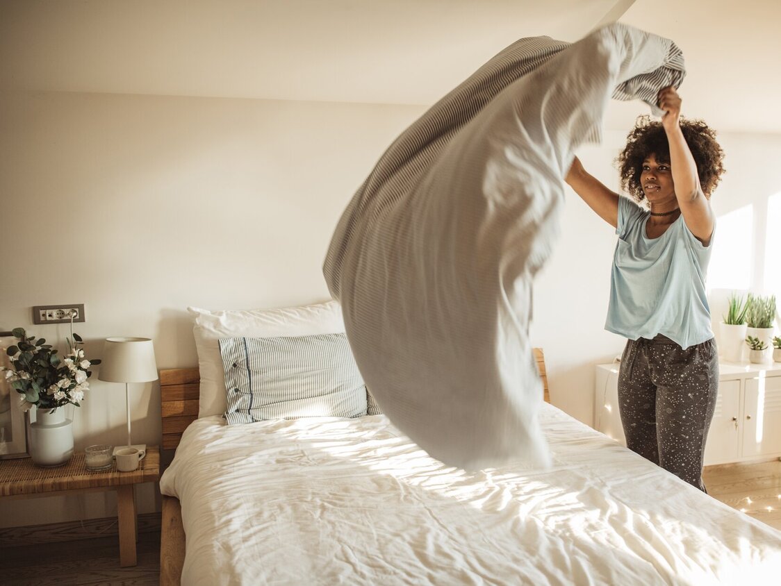 Eine Frau schüttelt die Bettdecke auf einem Bett auf.