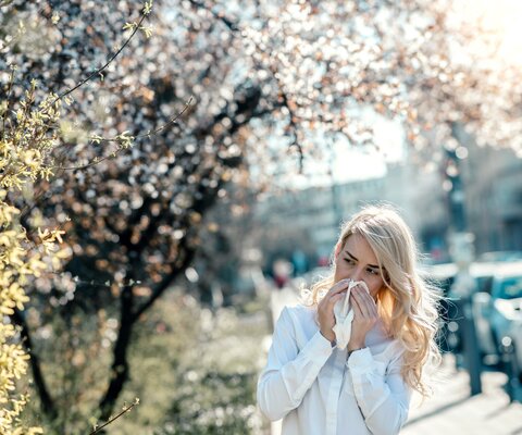 Eine blonde Frau läuft an blühenden Bäumen vorbei und niest.