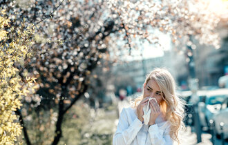Eine blonde Frau läuft an blühenden Bäumen vorbei und niest.