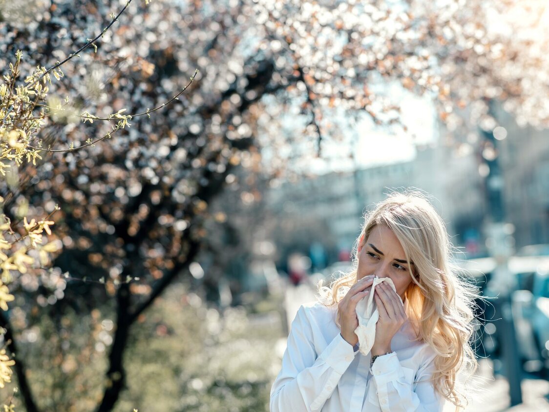 Eine blonde Frau läuft an blühenden Bäumen vorbei und niest.