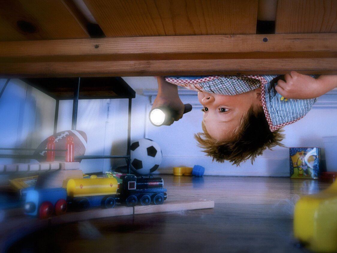 Ein Junge guckt mit einer Taschenlampe unter sein Bett.