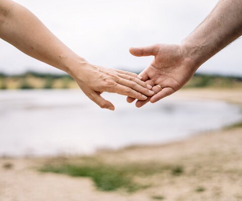 Zwei Hände berühren sich. Im Hintergrund sieht man einen See.