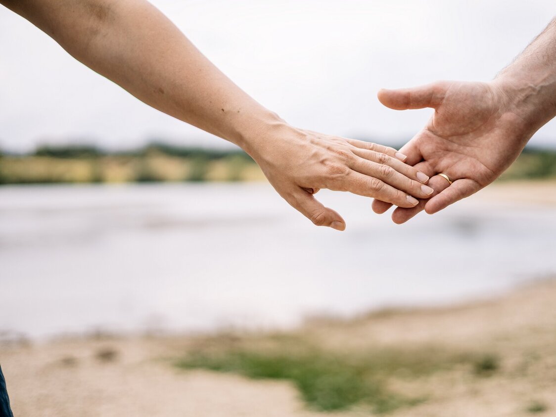 Zwei Hände berühren sich. Im Hintergrund sieht man einen See.