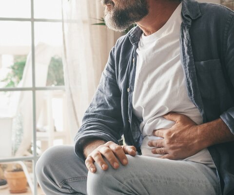 Ein Mann hält sich im Sitzen eine Hand an den Bauch.