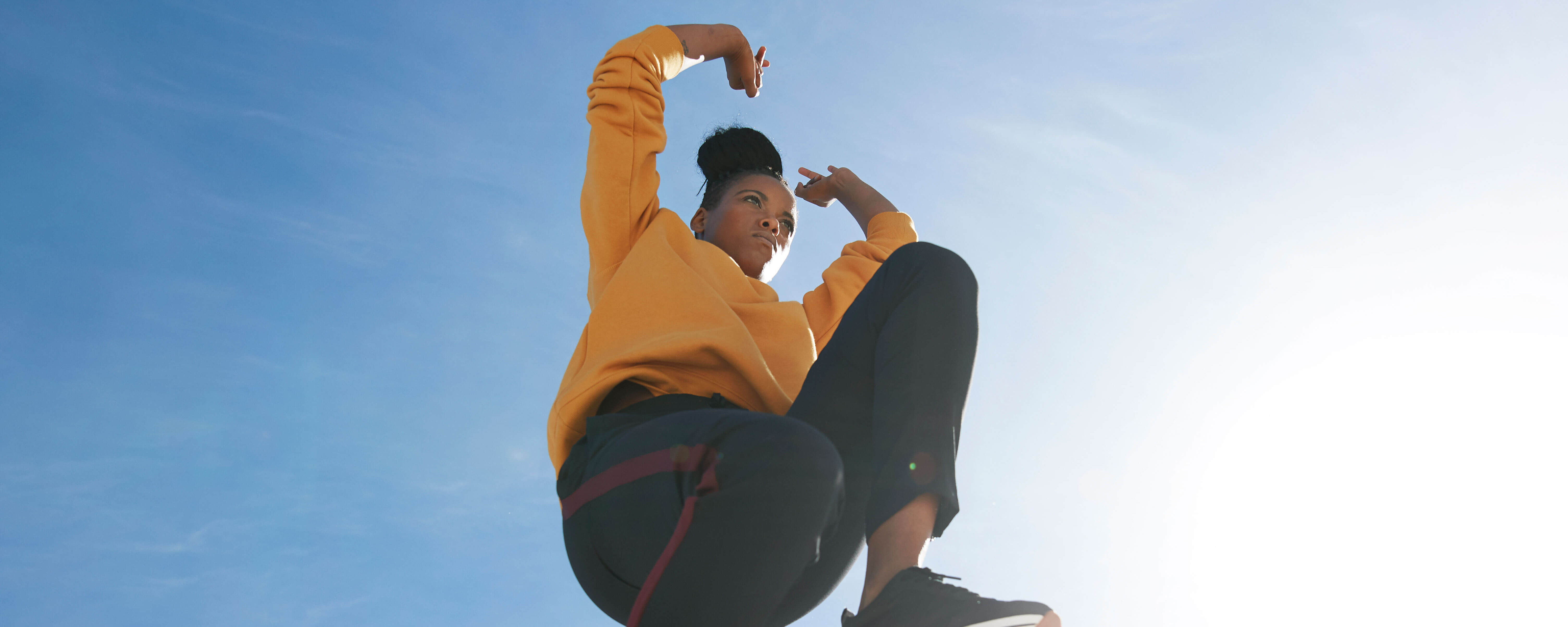 Junge Frau mit gelbem Pullover, die an einem sonnigen Tag gen blauem Himmel springt