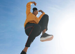 Junge Frau mit gelbem Pullover, die an einem sonnigen Tag gen blauem Himmel springt