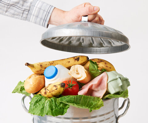 Hand packt Deckel auf Mülltonne voller Lebensmittelabfälle.