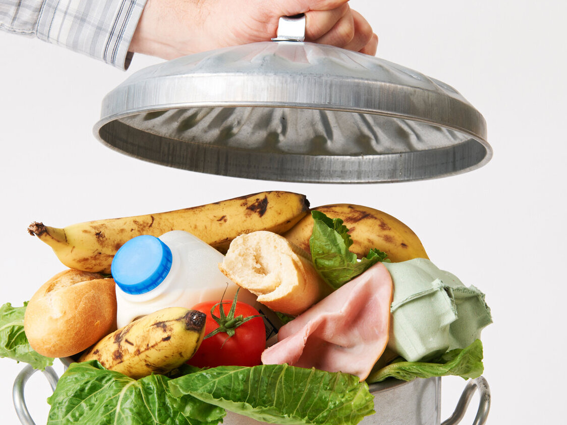 Hand packt Deckel auf Mülltonne voller Lebensmittelabfälle.