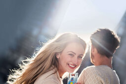 Ein junges Paar steht in der Stadt. Die Frau dreht sich zur Kamera und hält ihre Gesundheitskarte hin.