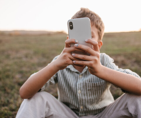 Gut gekleideter Junge, der auf einen Telefonbildschirm schaut