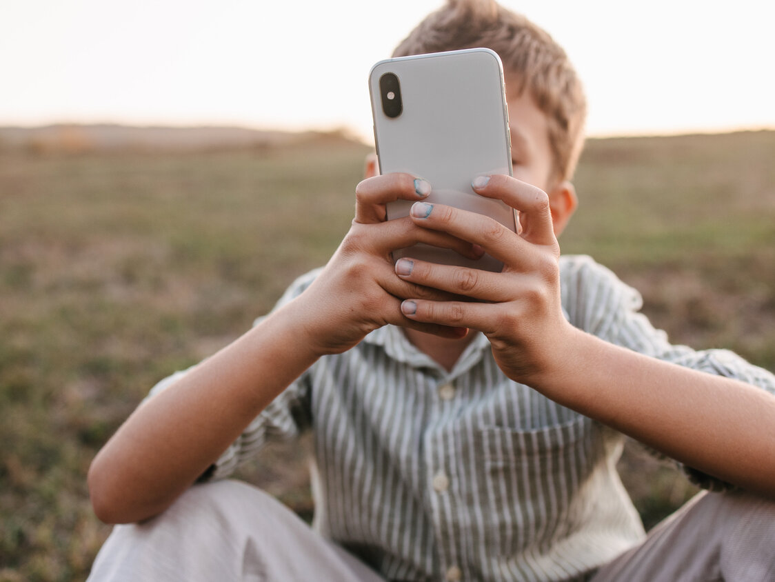 Gut gekleideter Junge, der auf einen Telefonbildschirm schaut
