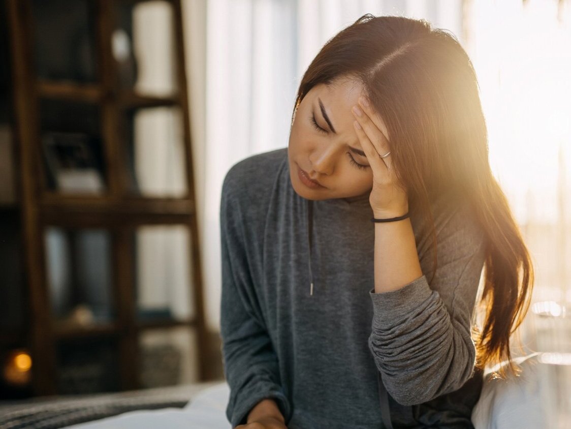Frau sitzt auf dem Bett mit Kreislaufproblemen