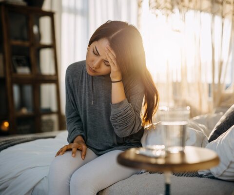 Frau sitzt auf dem Bett mit Kreislaufproblemen