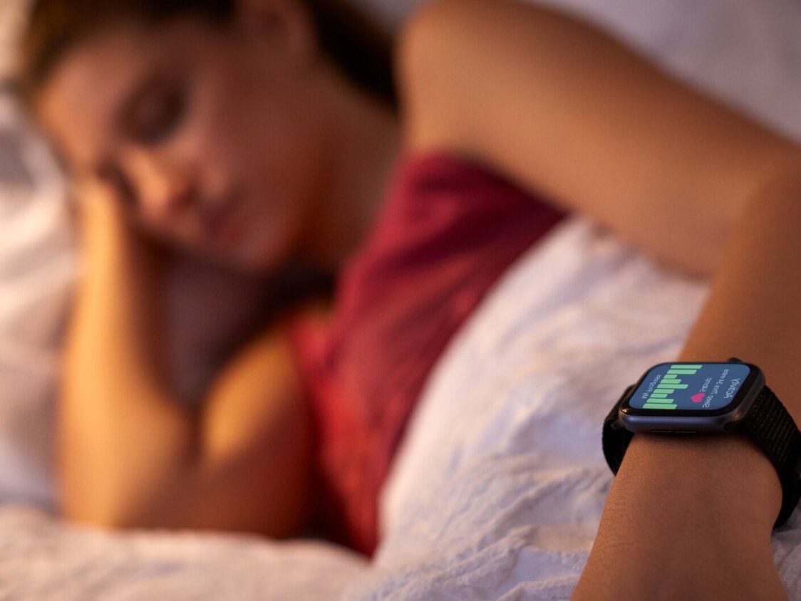 Eine Frau liegt im Bett und man sieht ihre aktive Smartwatch.