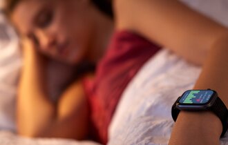 Eine Frau liegt im Bett und man sieht ihre aktive Smartwatch.