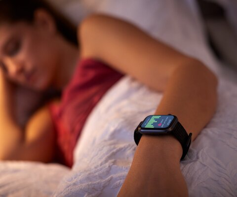 Eine Frau liegt im Bett und man sieht ihre aktive Smartwatch.