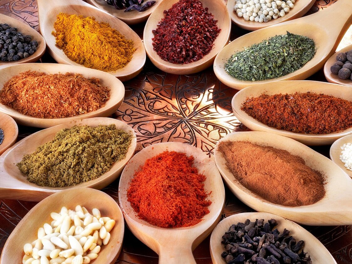 Gewürze und Kräuter in verschiedenen Farben werden auf Holzlöffeln präsentiert.