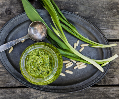 Frisches Bärlauch liegt neben einem Glas Pesto und einem Löffel auf einem ovalen Teller.