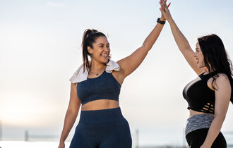 Women giving each other a high five after exercising at the beach