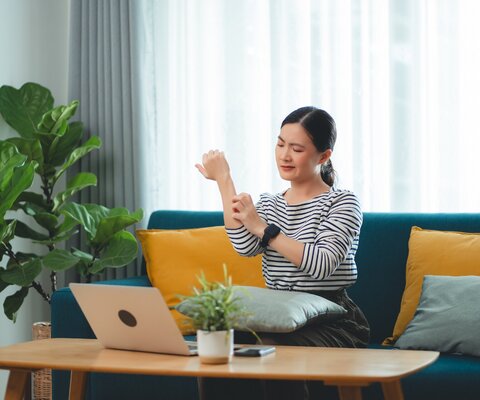 Eine Frau sitzt auf dem Sofa und kratzt sich am Arm.