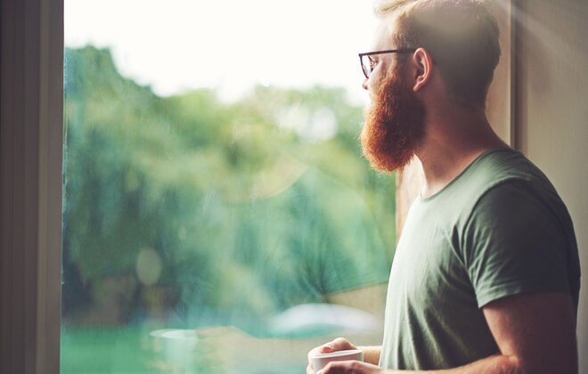 Ein Mann steht am Fenster und guckt nach draußen.