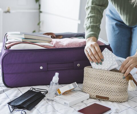 Frau bereitet Reisekoffer auf dem Bett zu Hause vor. Sie packt Medikamente und Desinfektionssachen für die Reise.
