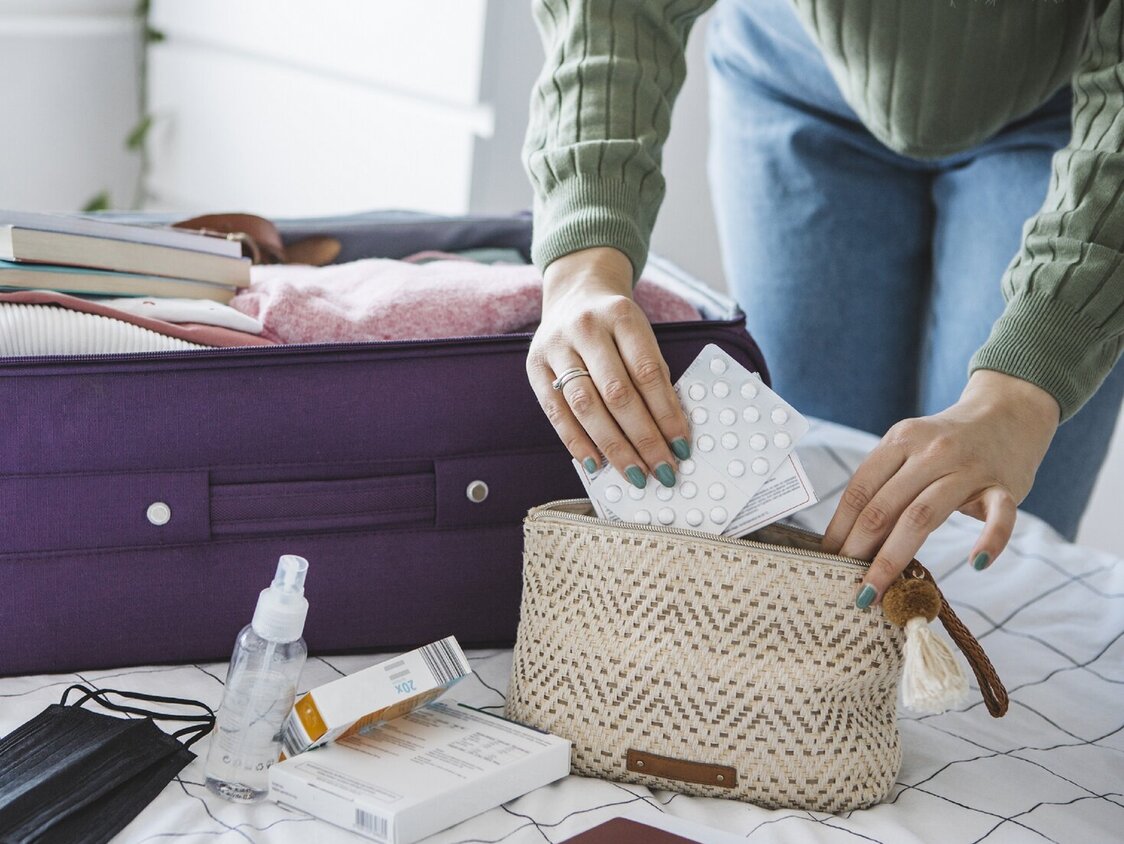 Frau bereitet Reisekoffer auf dem Bett zu Hause vor. Sie packt Medikamente und Desinfektionssachen für die Reise.