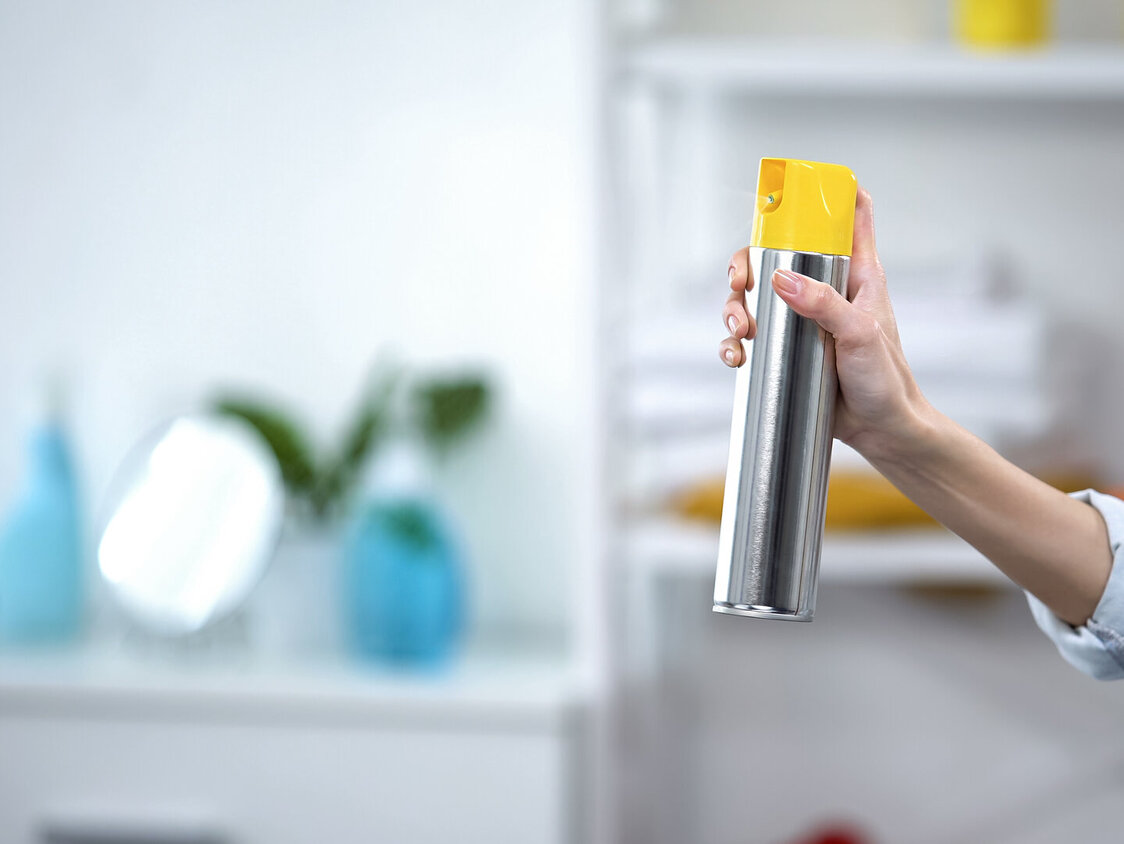 Eine Frauenhand sprüht Lufterfrischer im Zimmer.