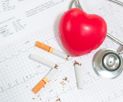 Auf einem ausgedruckten EKG-Diagramm liegen durchgebrochene Zigaretten, ein Herz-Luftballon und ein Stetoskop.