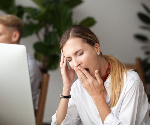 Eine Frau sitzt am PC und gähnt.