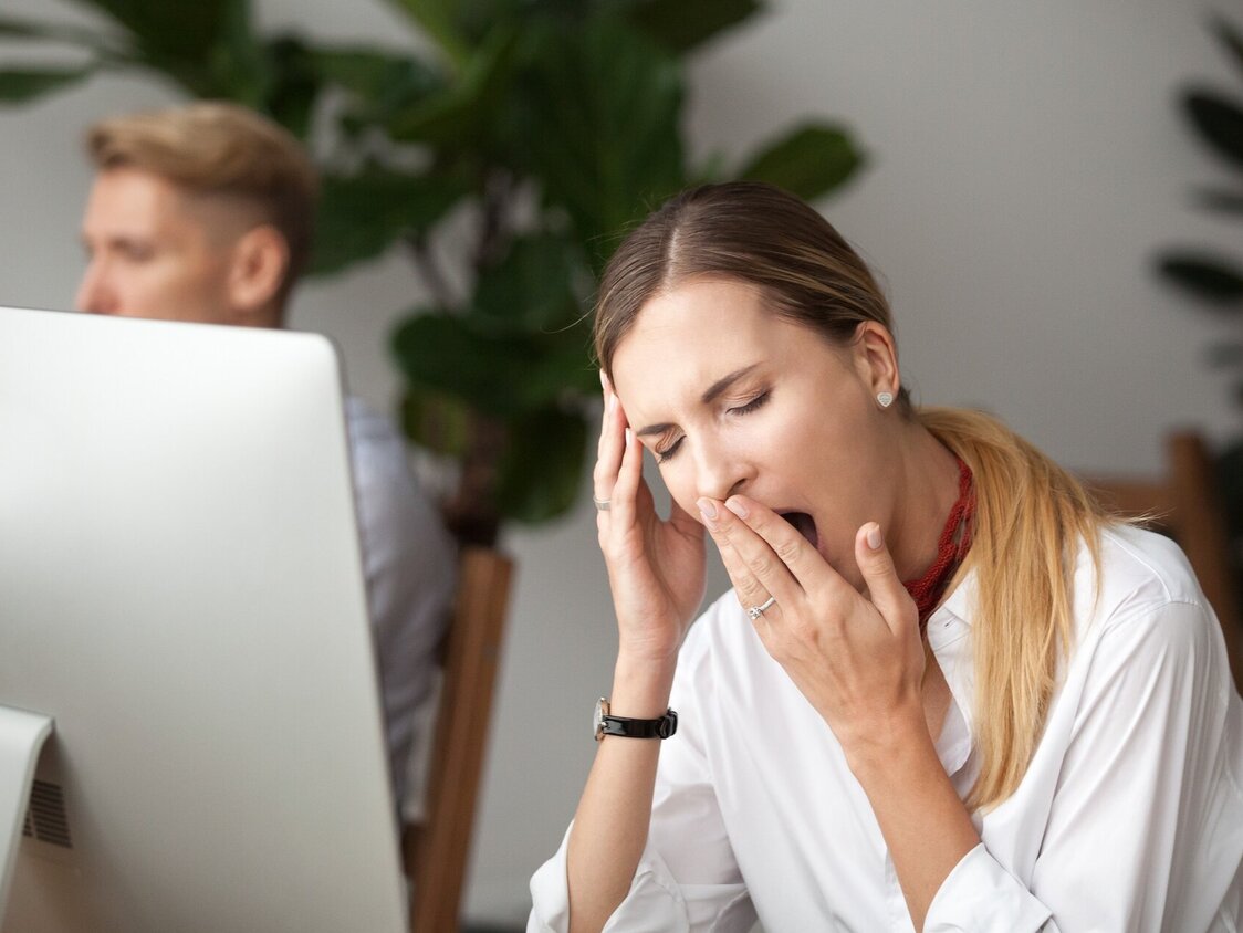 Eine Frau sitzt am PC und gähnt.