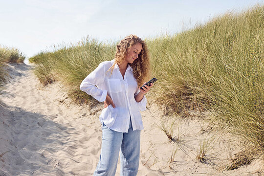 Eine Frau steht in einer Düne und guckt auf ihr Handy.