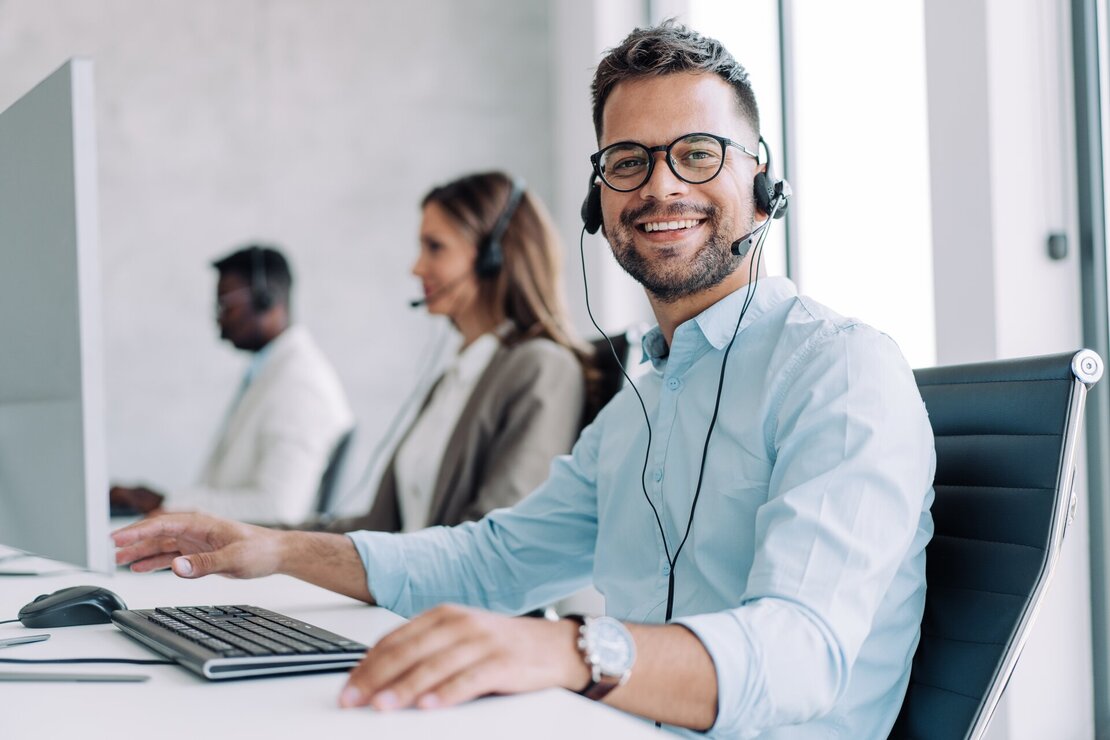 Mann im Callcenter mit Headset, der freundlich in die Kamera blickt