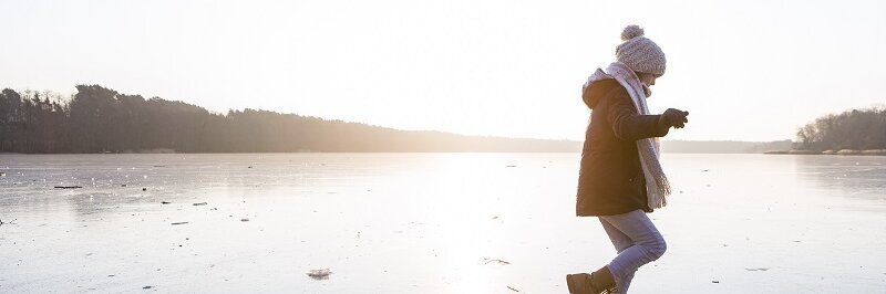 Kind in Winterkleidung läuft auf zugefrorenem See.