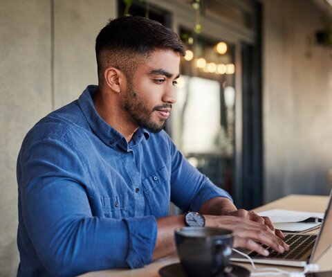  Ein Mann steht am höhenverstellbaren Tisch und arbeitet am Laptop.