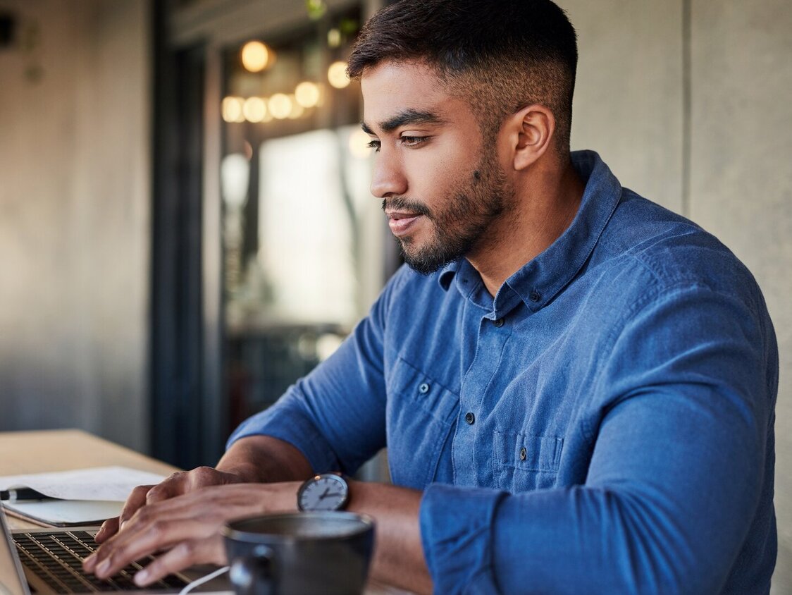  Ein Mann steht am höhenverstellbaren Tisch und arbeitet am Laptop.
