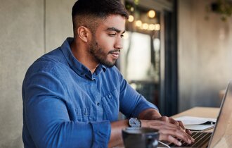  Ein Mann steht am höhenverstellbaren Tisch und arbeitet am Laptop.