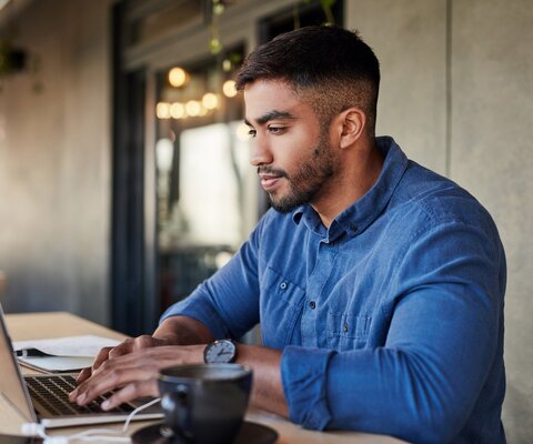  Ein Mann steht am höhenverstellbaren Tisch und arbeitet am Laptop.