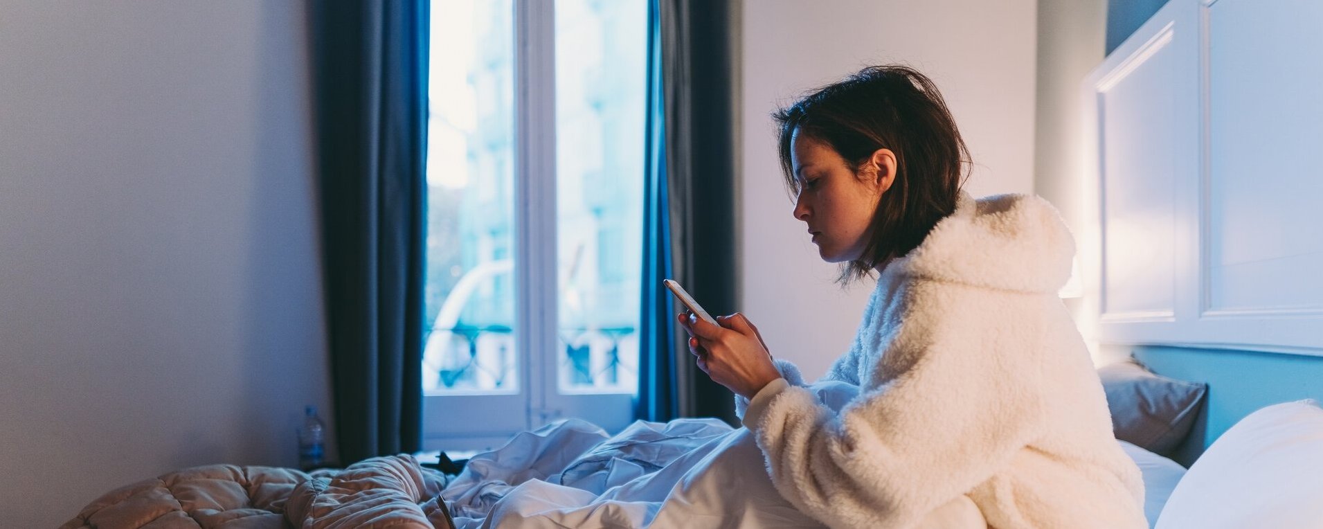 Eine Frau sitzt im Bett und schaut auf ihr Handy.