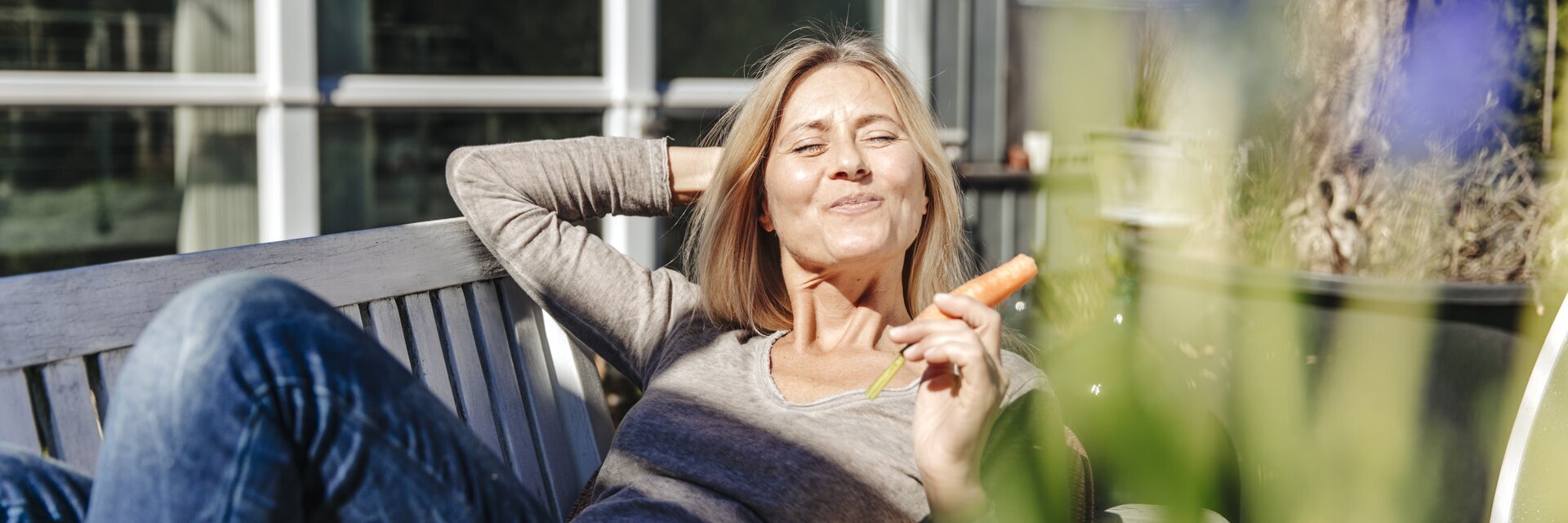 Eine Frau liegt auf einer Terrasse mit Jeans und T-Shirt und sonnt sich.