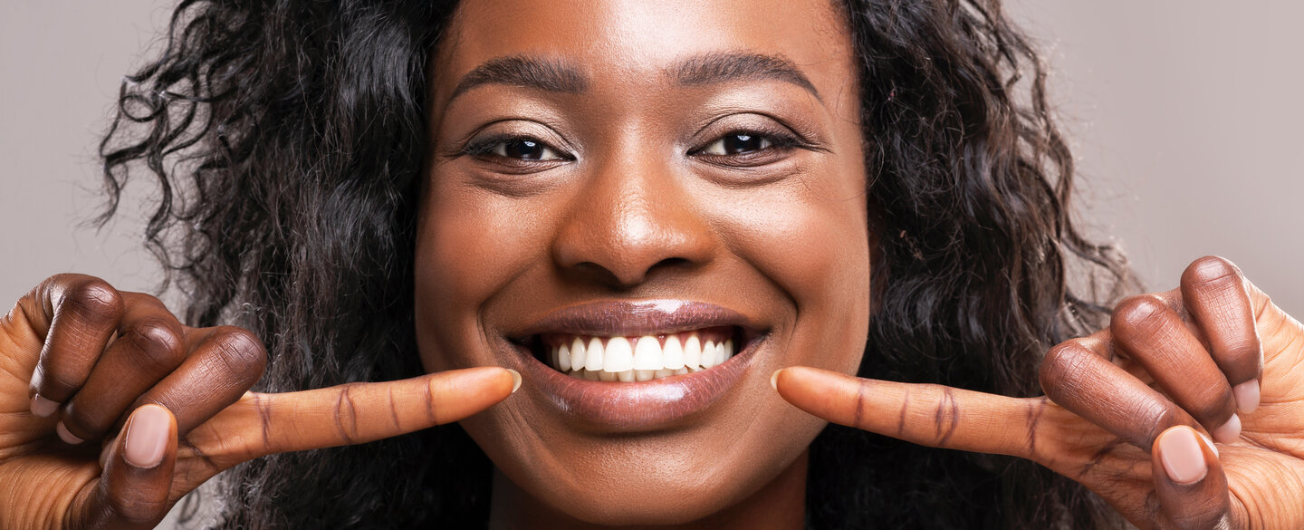 Eine farbige Frau zeigt auf ihre weißen Zähne.