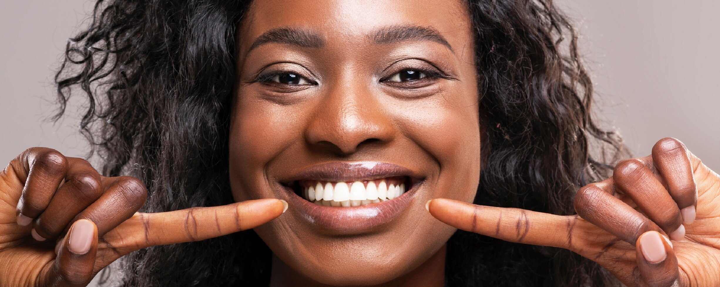 Eine farbige Frau zeigt auf ihre weißen Zähne.