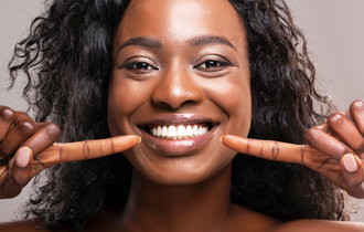 Eine farbige Frau zeigt auf ihre weißen Zähne.