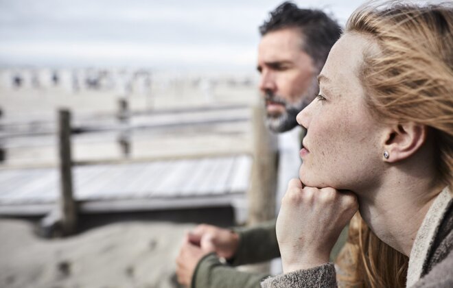 Eine Frau und ein Mann gucken am Strand in die Ferne.