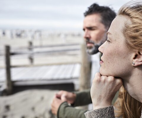 Eine Frau und ein Mann gucken am Strand in die Ferne.