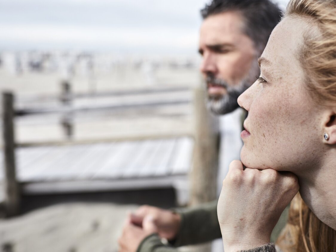 Eine Frau und ein Mann gucken am Strand in die Ferne.