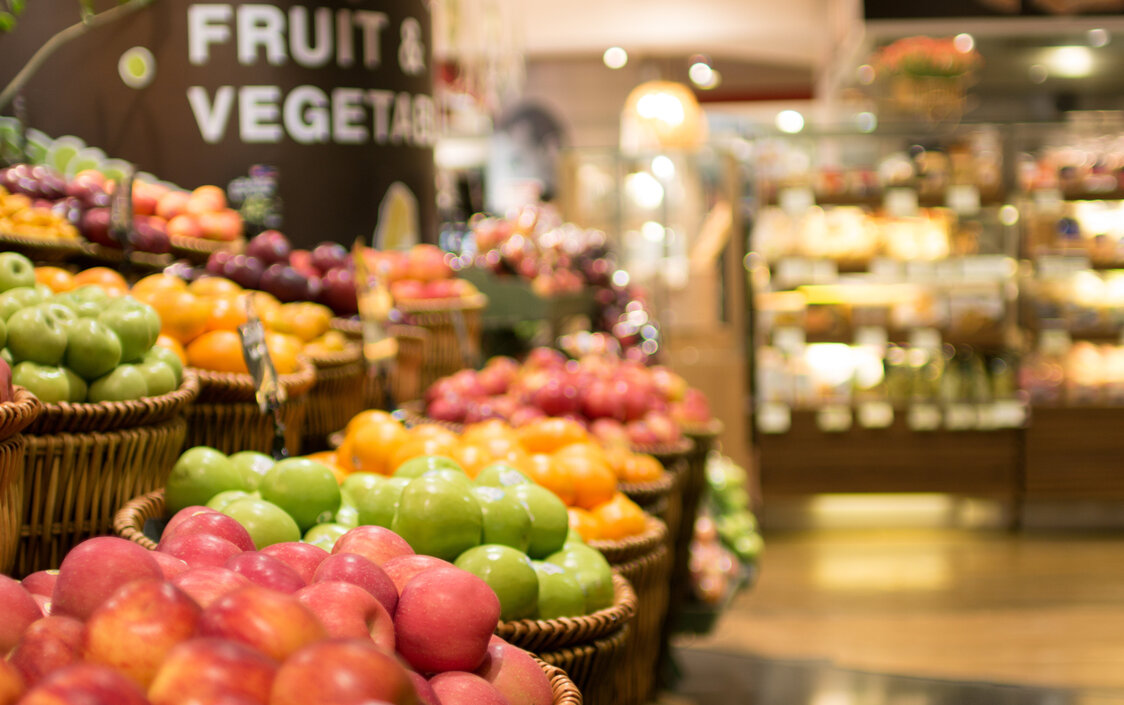 Es sind viele Körbe mit Äpfel in verschiedenen Farben im Supermarkt zu sehen.